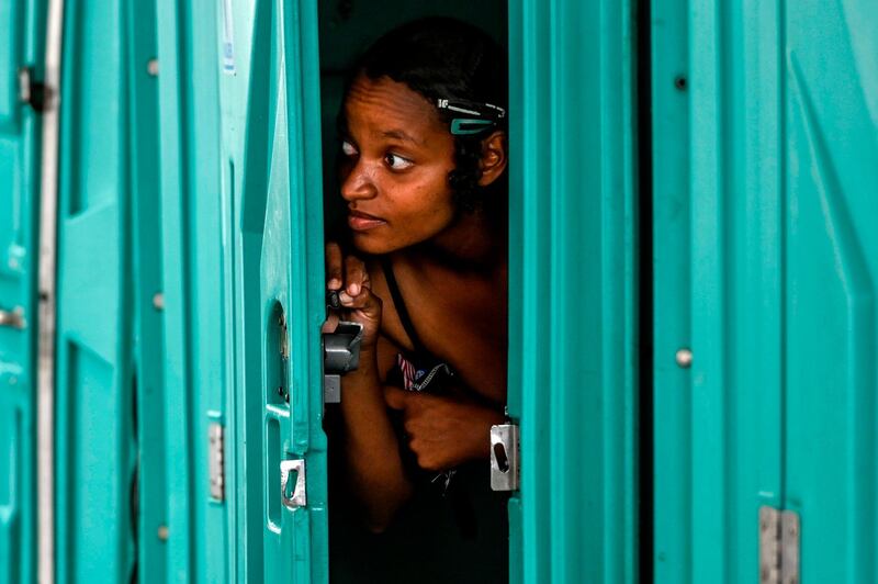 A woman looks out the door of a chemical bathroom cabin before taking a shower at an area provided for homeless people in Medellin, Colombia. AFP