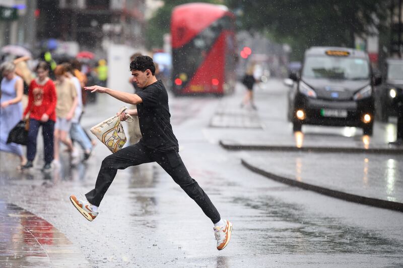 A man leaps over a puddle as shoppers rush through a heavy downpour in London. Getty Images