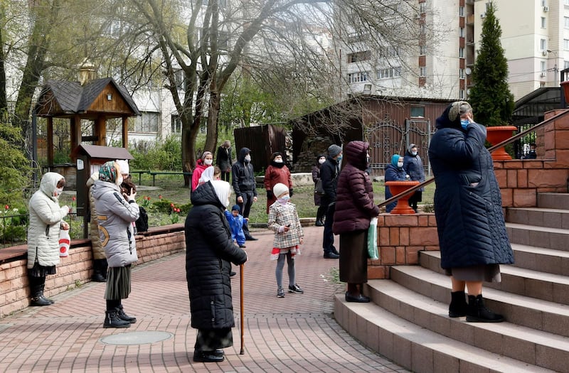 People wearing face masks to protect against coronavirus pray during a commemorative religious ceremony in front of the church at a memorial of the Chernobyl tragedy victims in capital Kiev, Ukraine.  AP