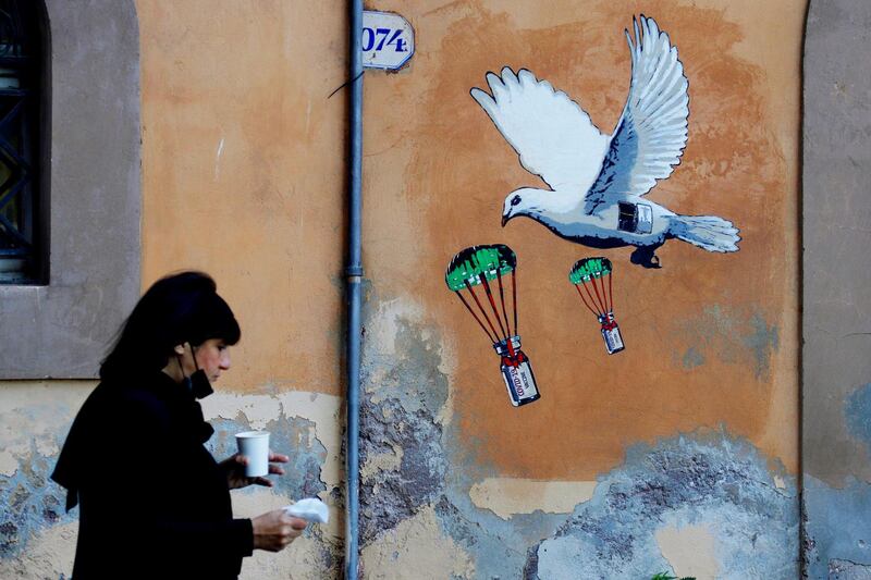A woman walks past a mural depicting a white dove parachuting Covid-19 vaccine vials, near the Italian health ministry headquarters in Rome. AP Photo