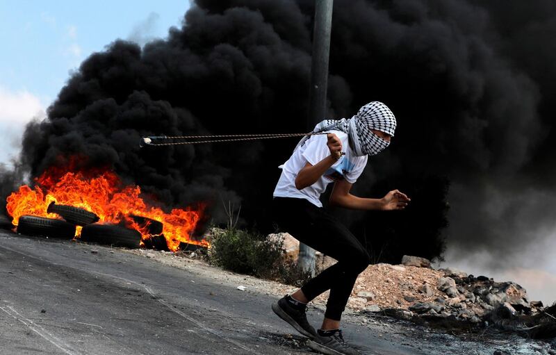 Smoke billows from burning tyres as a Palestinian protester uses a slingshot to hurl stones at Israeli troops in the village of Kfar Qaddum, in the Israeli-occupied West Bank. AFP