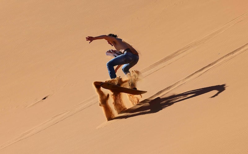 A tourist sandboards down a dune in the Dubai desert