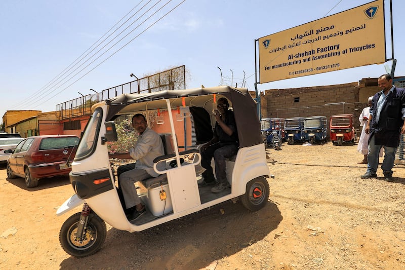 Workers test-drive a new electric tuk-tuk in the factory grounds.  