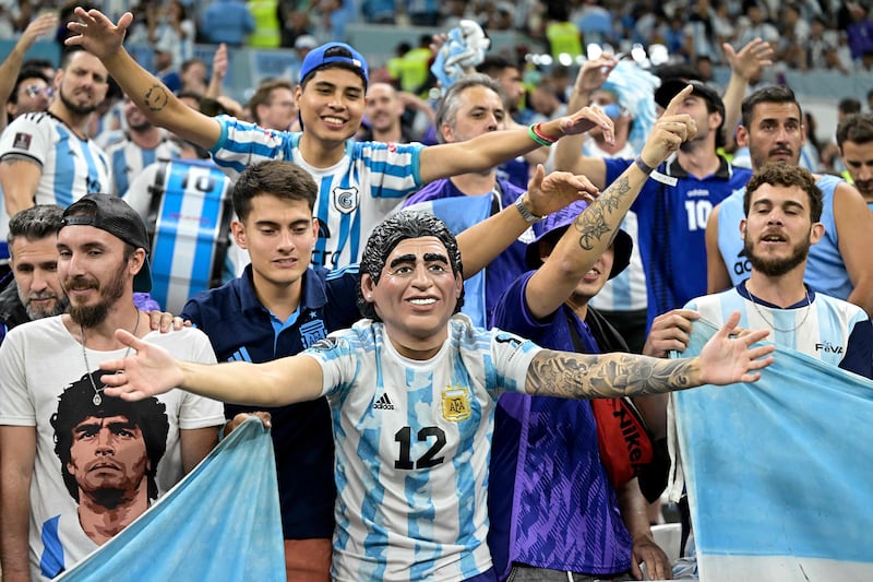Supporters of Argentina, one wearing a mask of the nation's late footballing great Diego Maradona, are in loud spirits in the stadium. AFP