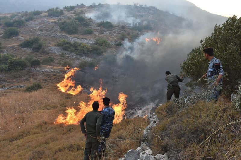A handout picture released by the official Syrian Arab News Agency (SANA) shows security forces walking on a burnt hill Ain Halaqim, in the western countryside of Hama Governorate, during fires. AFP