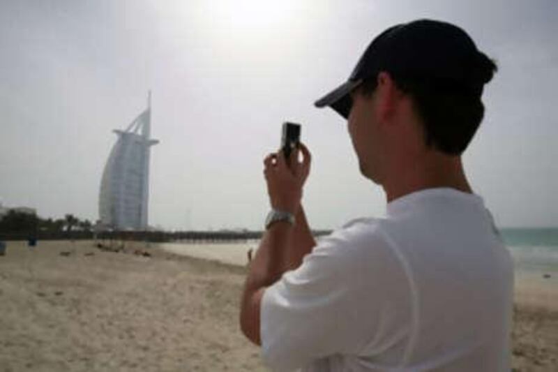 A tourist on the beach taking photos of the Burj al Arab hotel in Dubai.