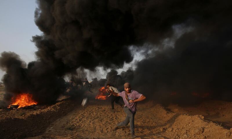 A protester hurls stones while others burn tires near the fence of the Gaza Strip border with Israel, during a protest east of Gaza City. AP Photo