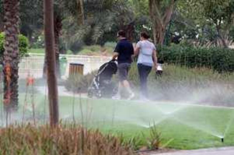 DUBAI, UNITED ARAB EMIRATES - APRIL 17:  People walk past water sprinklers in The Greens area of Dubai on April 17, 2009.  (Randi Sokoloff / The National)  For Stock-water usage/water waste and/or green space in the city-people relaxing, people walking.
 *** Local Caption ***  RS025-041709-STOCK.jpg