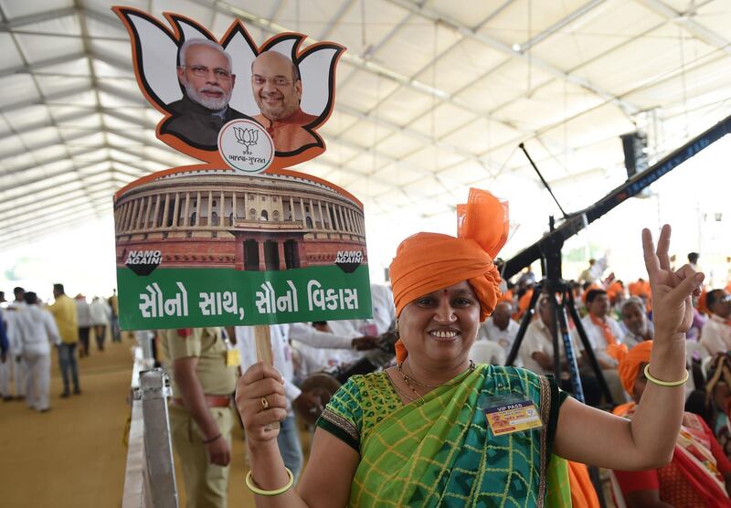 An Indian supporter of the Bhartiya Janta Party (BJP) carries a cut-out of the Indian Parliament with the images of Prime Minister Narendra Modi and BJP President Amit Shah during a rally in Amreli, some 250km from Ahmedabad, on April 18, 2019. More than 157 million of the 900 million electorate are eligible to cast ballots on the second of seven days of voting in the world's biggest election. / AFP / SAM PANTHAKY
