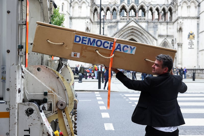A protestor against Ulez expansion pretends to put a coffin in to a rubbish truck outside the High Court. Reuters
