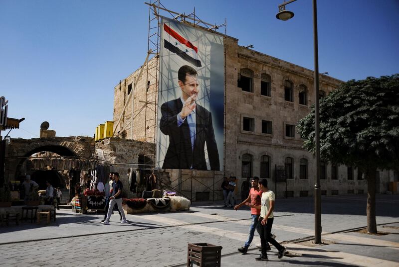 (FILES) In this file photo taken on September 27, 2019 during a guided tour with the Russian army shows men walking past a poster of Syrian President Bashar al-Assad in the old city of Aleppo. Syria is to hold a presidential election on May 26, the parliament speaker announced today, the country's second in the shadow of civil war, seen as likely to keep President Bashar Al-Assad in power. / AFP / Maxime POPOV
