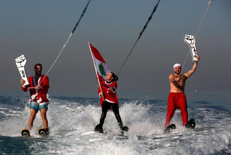 Members of a Lebanese water sports club dressed as Santa Claus wave a national flag and  cardboard cut-outs of a clenched fist reading “Revolution” to show support to ongoing anti-government protests, as they water-ski in the bay of Jounieh north of the capital. AFP