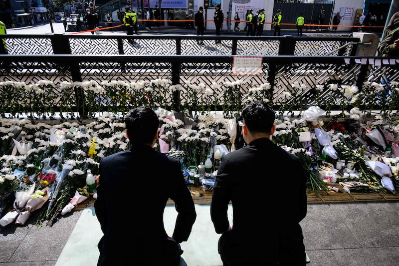 Two men kneel down to pay their respects at a makeshift memorial outside a subway station in Itaewon district. AFP