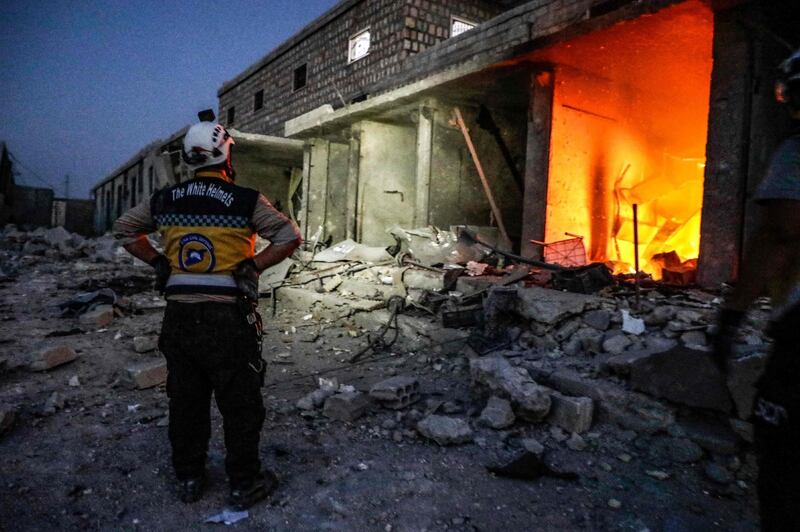 A member of the Syrian Civil Defence, also known as the "White Helmets", stands outside a burning shop following a reported air strike in Kfar Ruma in Syria's northwestern Idlib province. AFP