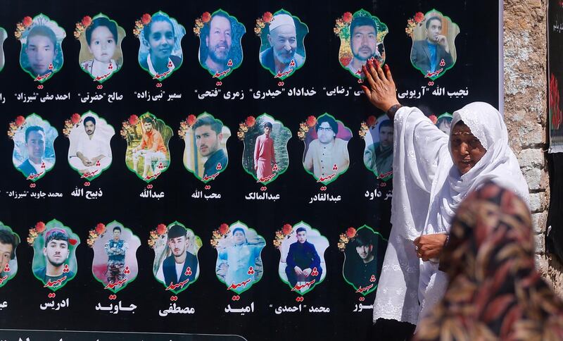 An Afghan woman cries as she touches a banner displaying photographs of victims of the Dubai City wedding hall bombing during a memorial service in Kabul, Afghanistan, Tuesday, Aug. 20, 2019. The deadly bombing at a wedding in Afghanistan's capital late last Saturday that killed dozens of people was a stark reminder that the war-weary country faces daily threats not only from the long-established Taliban but also from a brutal local affiliate of the Islamic State group, which claimed responsibility for the attack. (AP Photo/Rafiq Maqbool)