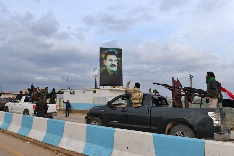 A convoy of pro-Syrian government fighters flashing the victory gesture as they ride through the windows of pickup trucks upon arriving in Syria's northern region of Afrin, with a portrait of the Kurdistan Worker's Party (PKK) leader Abdullah Ocalan seen on a banner in the background. George Ourfalian / AFP