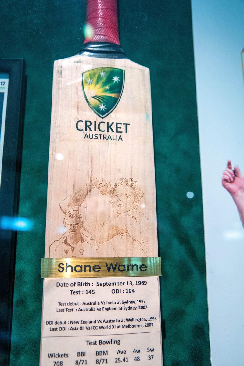 A cricket bat displays Shane Warne statistics.