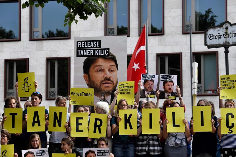 (FILES) This file photo taken on June 15, 2017 shows Amnesty International activists holding  a portrait of the head of Amnesty International in Turkey, as they stage a protest against his detention in Turkey, in front of the Turkish Embassy in Berlin.
An Istanbul court on January 31, 2018 ordered the conditional release of Taner Kilic, the head of Amnesty International in Turkey. A total of 11 activists including Kilic went on trial in Istanbul on terror charges which the rights watchdog said were "baseless allegations". 
 / AFP PHOTO / John MACDOUGALL