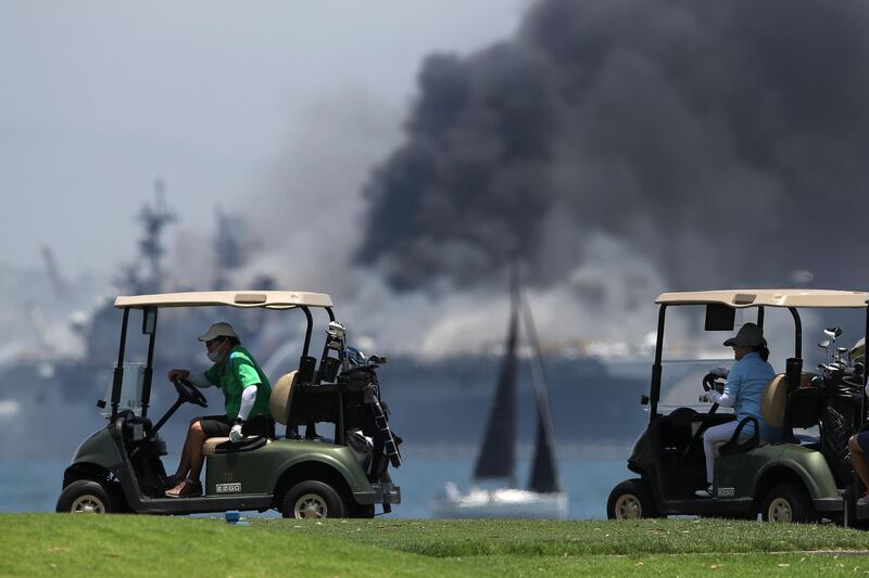Golfers play on as a fire rages on the amphibious assault ship 'USS Bonhomme Richard' at the naval base in San Diego, California. Getty Images