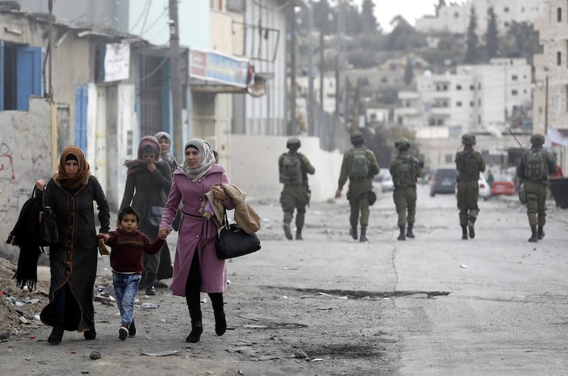 epa06411051 Palestinian women pass as Israeli army soldiers take position during clashes in al-Fawwar refugee camp, south of the West Bank city of Hebron, 31 December 2017. Clashes erupted as ongoing protests were held against US President Trump's 06 December announcement he is recognizing Jerusalem as the Israel capital and will relocate the US embassy from Tel Aviv to Jerusalem.  EPA/ABED AL HASHLAMOUN