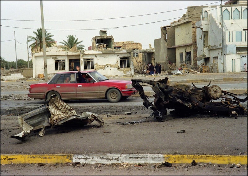 An Iraqi car (L) drives 17 fevruary 1991 along the main street of Samawa, a city 250 kms south from Baghdad, as the wreckage of a car destroyed during an allied bombing raid lies on the ground. Iraq's invasion of Kuwait 02 August 1990, ostensibly over violations of the iraqi border, led to the Gulf War which began 16 january 1991. A US-led multi-nationalforce repulsed Iraq from Kuwait and a cease-fire was signed 28 february 1991. (Photo by MIKE NELSON / AFP)