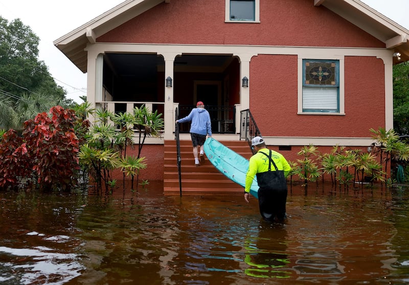 A man helps his neighbour carry a kayak on to his porch through flooded streets. AFP