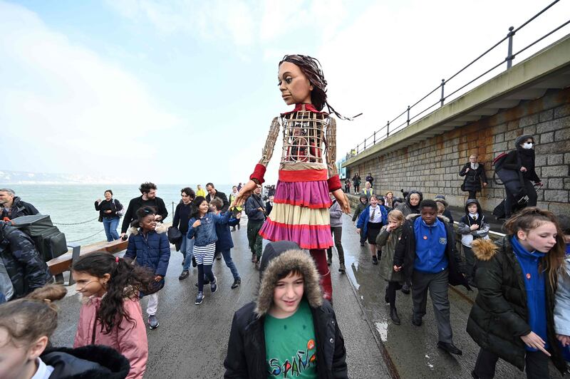 Little Amal walks along the sea front at the harbour in Folkestone with local children. AFP