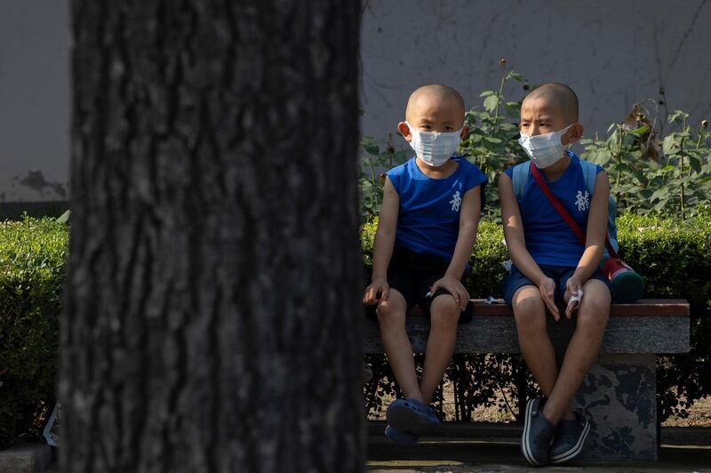 Children wearing masks to curb the spread of the coronavirus sit on a bench in Beijing, China. China reported only a handful of new cases of the virus, all of them brought from outside the country, as domestic community infections fall to near zero. AP Photo