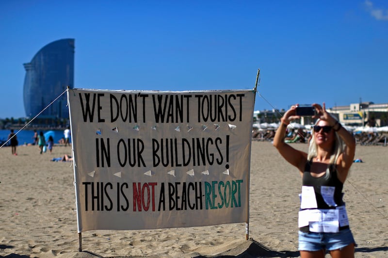 A woman takes a picture during a protest against tourism in Barcelona, Spain, Saturday, Aug. 12, 2017. The residents claim that the influx of tourists has increased the price of rents and produced a spike in rowdy behavior by party-seeking foreigners. The protest comes amid growing tension between governmental authorities and radical leftist groups after they launched a campaign of vandalism against mass tourism in Barcelona and other parts of Spain. The banner reads in Catalan: "For the abolition of tourist floors." (AP Photo/Manu Fernandez)