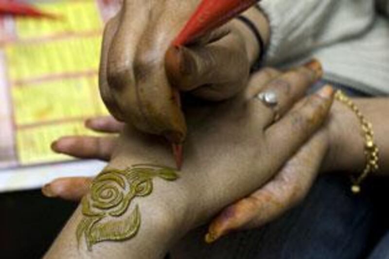 A salon manager applies red henna, which is less likely to contain large proportions of the chemical PPD, to a customer.