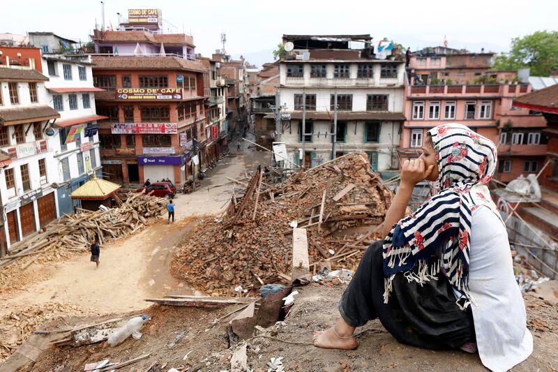 A woman sits on the top of a damaged temple in Kathmandu as she watches rescue workers search for victims of a 7.8 magnitude quake that struck in April 2015, killing more than 8,900 in Nepal, India, China and Bangladesh