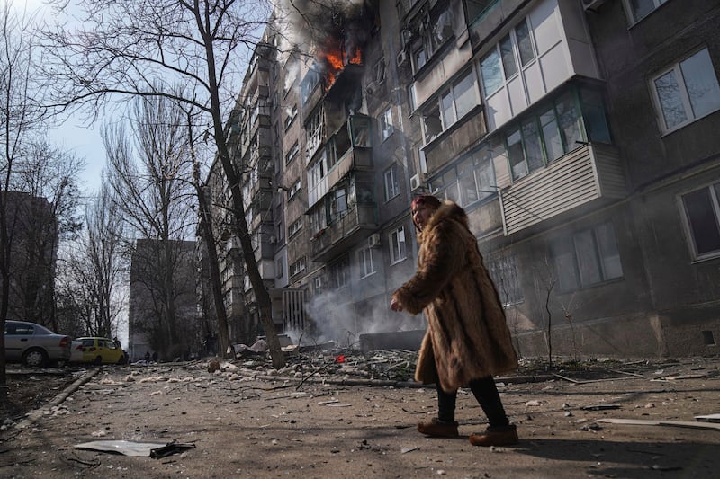 A woman walks past a burning apartment building after shelling. AP Photo
