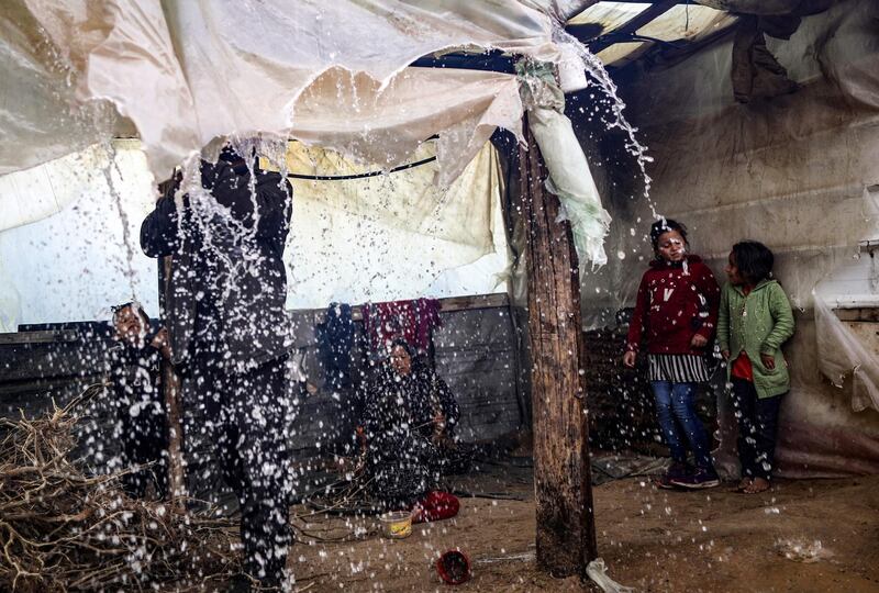 A Palestinian man pokes the nylon sheets covering the roof of his tent to remove the accumulating rain water, as children watch, on a rainy day in al-Amal (hope in Arabic) neighbourhood of Beit Lahia in the northern Gaza Strip.  AFP