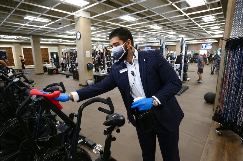 Kam Garlick, a sales manager at Life Time health club, disinfects exercise equipment as the full service facility remains open even as Arizona Gov. Doug Ducey has issued an executive order for all gyms to close due to the surge in coronavirus cases in Arizona Thursday, July 2, 2020, in Phoenix. For the third straight day, several health clubs in metro Phoenix were defying Ducey's 30-day shutdown order to close gyms, bars, water park and tubing businesses, raising questions about whether officials who have been criticized for responding indecisively to the pandemic will be effective in shutting down the clubs. (AP Photo/Ross D. Franklin)
