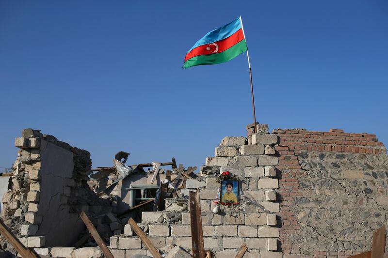 A portrait of a victim hangs on a house in a residential area destroyed by rocket fire by Armenian forces in Ganja, Azerbaijan, Friday, Nov. 27, 2020.  Azerbaijan's president has vowed to rebuild and revive the Kalbajar region, which Armenian forces ceded in a truce that ended six weeks of intense fighting over Nagorno-Karabakh. (AP Photo/Emrah Gurel)