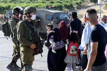 A woman walks past Israeli troops standing guard as Israeli settlers climb a hill reportedly to establish constructions for a new settlement in the town of Halhul, north of the West Bank city of Hebron. EPA