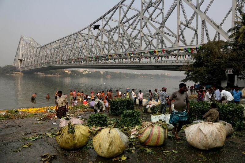 Sacks of foliage for decorations are kept on the bank for watering as people bathe in River Hooghly beside the heritage landmark Howrah Bridge, in Kolkata, India. Bikas Das / AP Photo