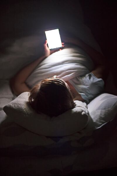 Woman looking up social medial at late night lying in bed, Internet addicted. Getty Images