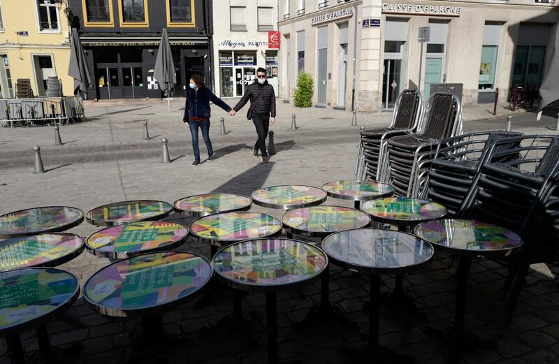 A couple pass a closed cafe in Lille, northern France, where festive gatherings will be banned and all bars required to close after the numbers of coronavirus infections rapidly increased. AP Photo