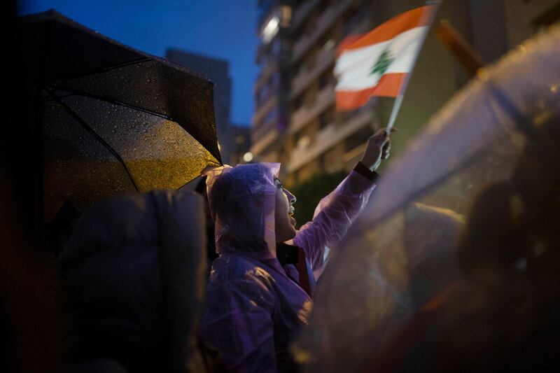 A Lebanese anti-government protester waves the national flag during in heavy rain outside of the residence of Lebanon's Prime Minister-Designate Hassan Diab in Beirut. AP Photo