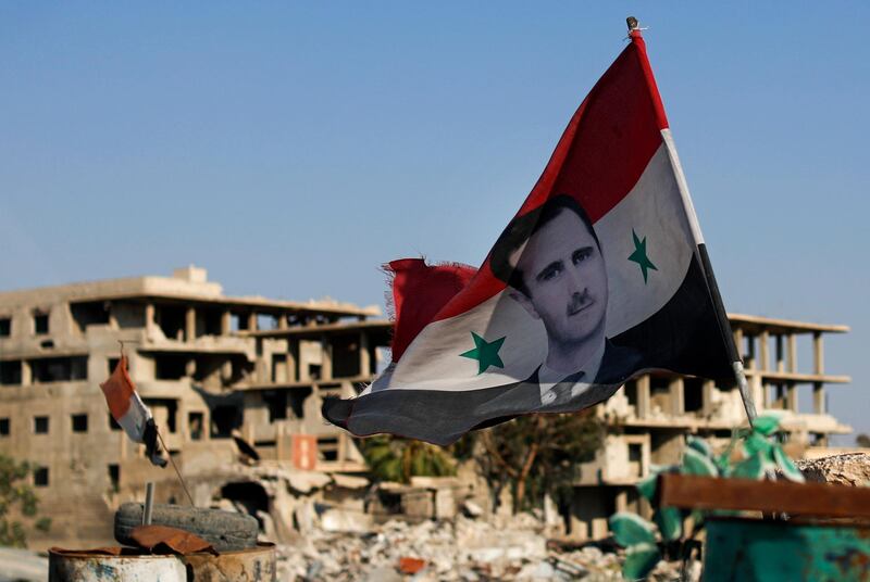FILE - In this July 15, 2018 file photo, a Syrian national flag with a picture of Syrian President Bashar Assad flies at an Army check point, in the town of Douma in the eastern Ghouta region, near Damascus, Syria. Assad has granted general amnesty to military deserters both within Syria and those outside the country in a decree published by state media on Tuesday, Oct. 9, 2018. The amnesty could help boost the return of refugees, some of whom have not been able to go back home because they were blacklisted. (AP Photo/Hassan Ammar, File)