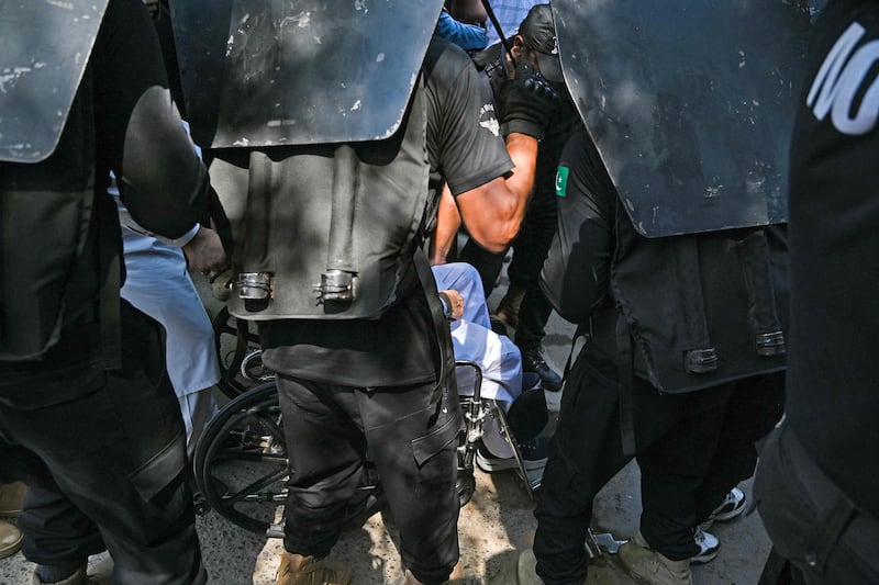 The guards apparently protected Mr Khan, seen sitting in a wheelchair, from protesters. He was later arrested. AFP
