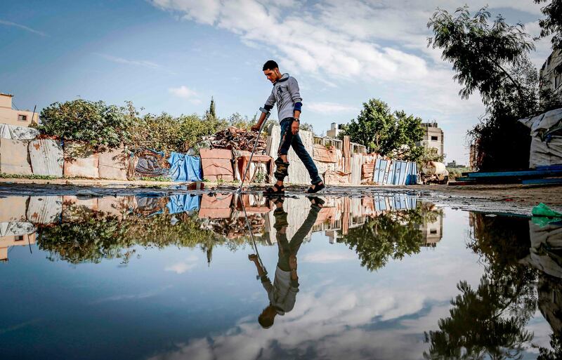 Murad al-Wadyah, a Palestinian youth who was previously injured in a prior demonstration, walks with a crutch past a rainwater pool near his home in Gaza City.  AFP