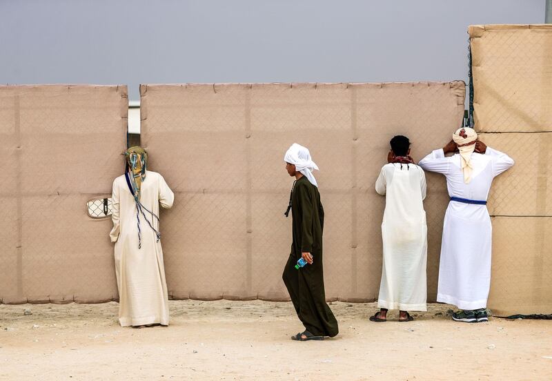 Abu Dhabi, United Arab Emirates, December 11,2019.    -- Camel fans take a sneak peek on gaps on the fence at the Al Dhafra Camel Festival 2019.Victor Besa/The NationalSection:  NAReporter:  Anna Zacharias