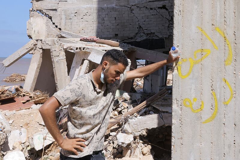 A rescue volunteer catches his breath. The Arabic graffiti reads 'Derna is gone'. Reuters
