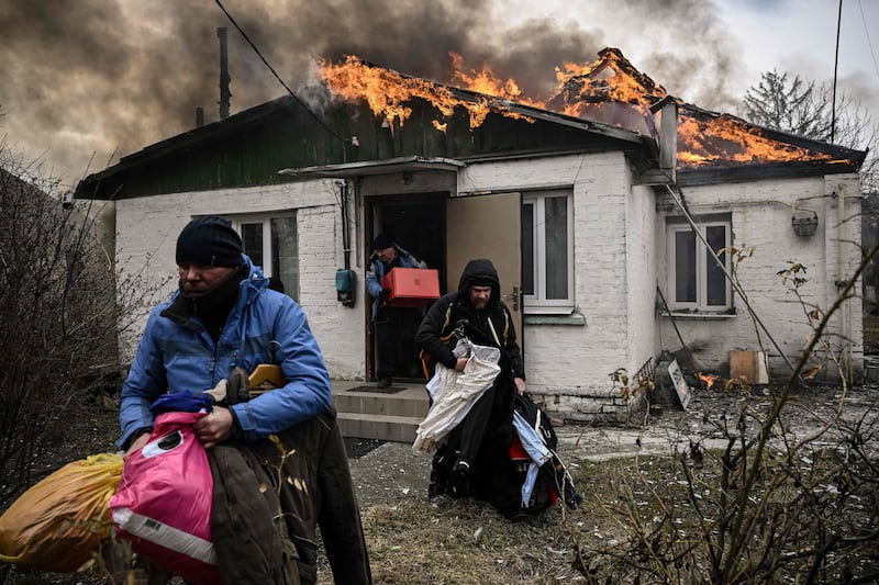 People remove personal belongings from a burning house after being shelled in Irpin. AFP