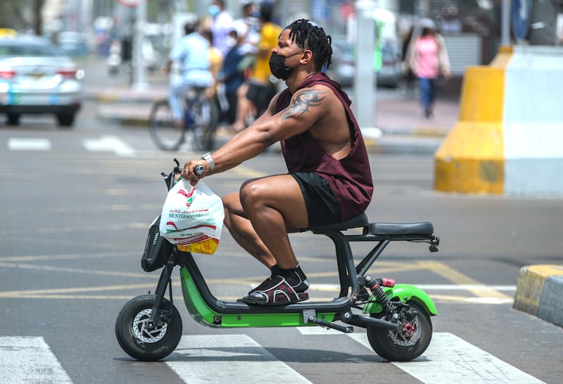 A rider on a seated e-scooter crosses Abu Dhabi's Hamdan Street in 2021. Riders are required by law to wear a helmet, and since this photo was taken, seated scooters have been banned. Victor Besa / The National