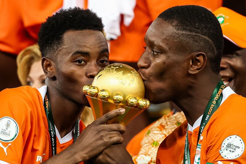 Ivory Coast forward Max-Alain Gradel, right, and teammate Simon Adingra kiss the Africa Cup of Nations trophy on the podium. AFP