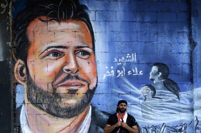 Ghayath al-Rawbeh, a Palestinian refugee who fled the Syrian crisis, poses on November 14, 2019 in front of a mural he painted of late Lebanese protester Alaa Abou Fakhr, who was shot dead south of Beirut two days ago, on a wall in the northern Lebanese city of Tripoli. The 38-year-old man died of gunshot wounds after the army opened fire to disperse protesters south of the Lebanese capital, in the second such death since the start of the largely peaceful protests. / AFP / Ibrahim CHALHOUB
