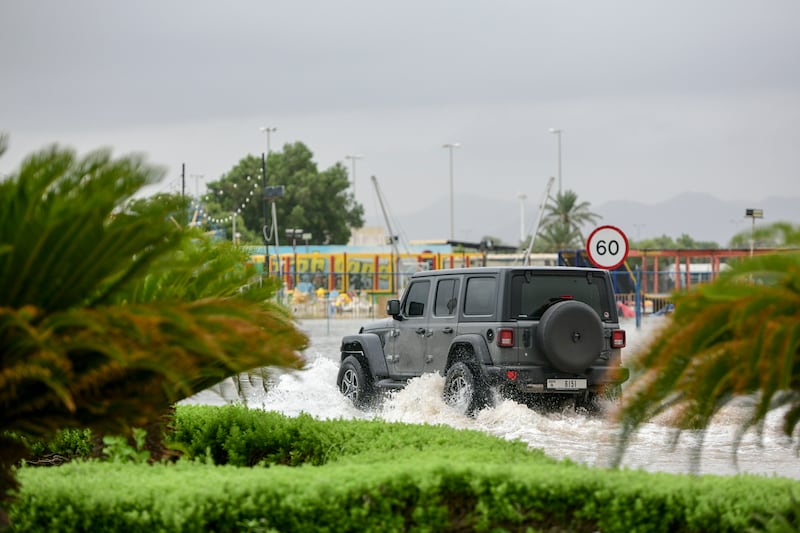 A car makes its way through floodwaters . Khushnum Bhandari / The National